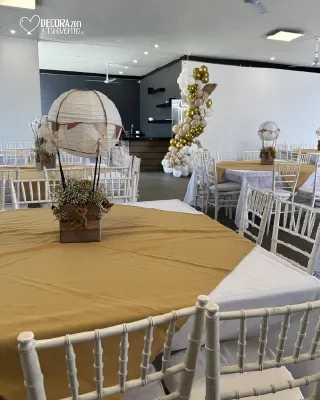 Salón con mesas redondas de mantel dorado, sillas Chiavari blancas y centros de globo aerostático